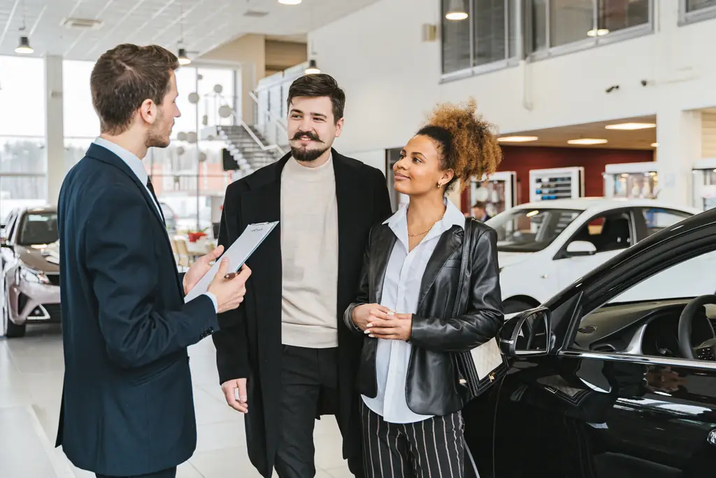 Vertex AutoCare agent explaining car repair coverage options to a couple at a car dealership